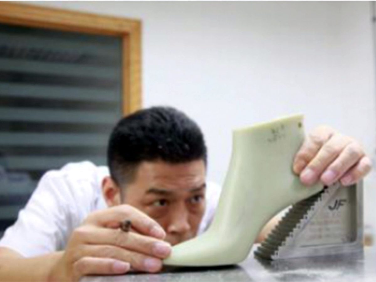 A technician checking the shape of a shoe last by hand.
