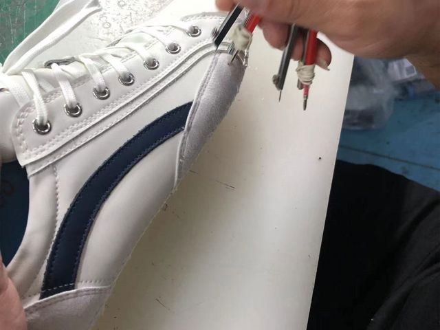 At one of our partner factories: a hand marking a detail on a white sneaker upper during a check.