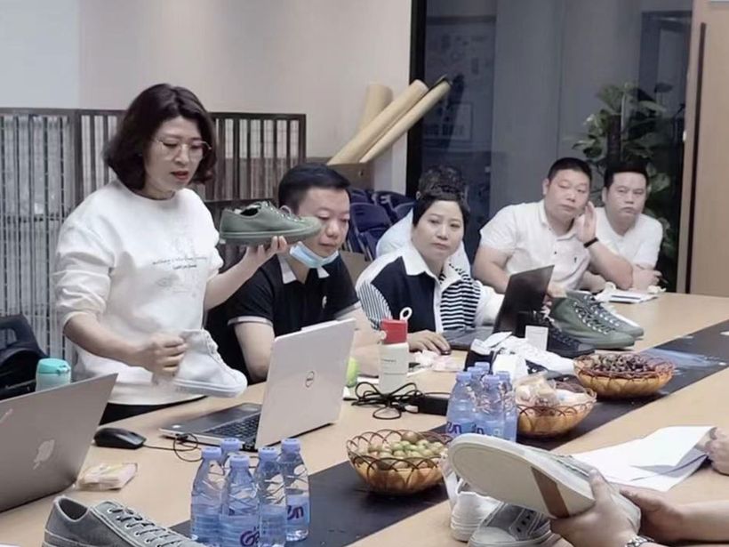 The KicksCo team around a meeting table, reviewing sample shoes and laptops.